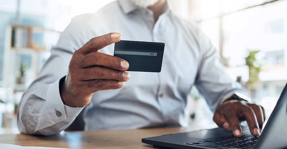 Person holding a credit card while using a laptop, symbolizing optimizing your TikTok profile for business success